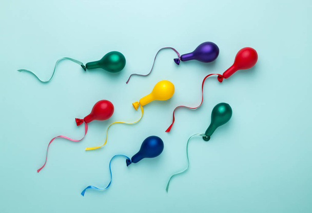 Colorful balloons in spermatozoid shape on blue. Trendy bright colors, minimal style. Sperm motion, donation concept. Abstract flat lay.  - Foto, imagen