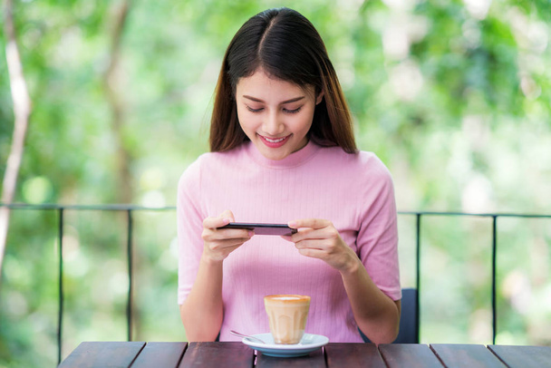 Asian lady use mobile phone in coffee shop with green nature background - Fotó, kép