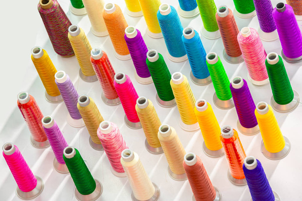 Colorful thread spools on rack. Used in fabric and textile industry. The concept of sewing production. - Photo, Image
