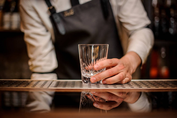 Bartender holding a beautiful oranate glass on the bar counter ready to prepare a fresh summer cocktail - Фото, зображення