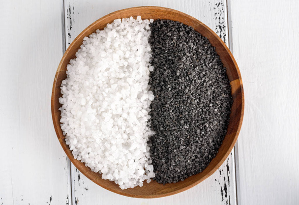 zwei Arten von Salz. weißes Meersalz und schwarzes Himalaya-Salz in einer Holzschale auf weißem Hintergrund. - Foto, Bild
