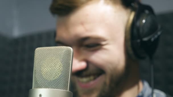 Portrait of male singer in headphones smiling at sound studio during working process. Young man emotionally recording new song. Working of creative musician. Show business concept. Slow motion - Materiaali, video