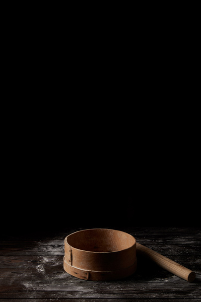 closeup shot of sieve and rolling pin on wooden table covering by flour isolated on black background  - Photo, Image