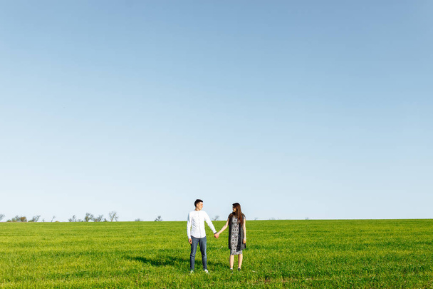 młody, szczęśliwy, kochający para, stojąc w zielone pola, na tle nieba przez ręce i cieszyć się sobą, reklama, - Zdjęcie, obraz