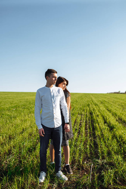 a young, happy, loving couple, standing in a green field, against the sky by the hands , and enjoy each other, advertising, - Photo, Image