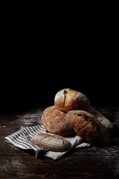 closeup view of various types of bread and sackcloth on wooden table covering by flour isolated on black background - Photo, Image