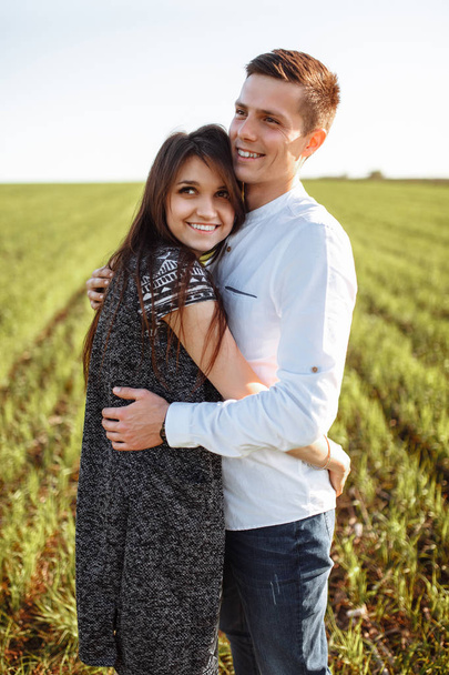 a young, happy, loving couple, standing in a green field, against the sky by the hands , and enjoy each other, advertising, - Foto, Imagen