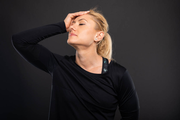 Portrait de gymnaste femme entraîneur tenant la tête comme blesser sur fond noir
 - Photo, image