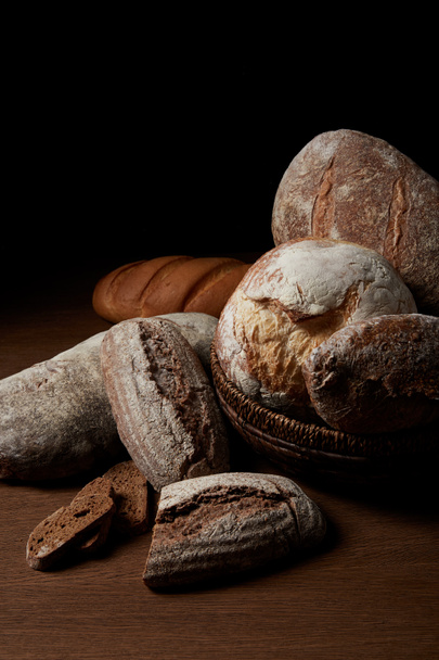 Detailní záběr různých druhů chleba a proutěný obilnice na dřevěný stůl  - Fotografie, Obrázek