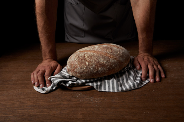cropped image of male baker standing near table with bread and sackcloth  - Fotografie, Obrázek