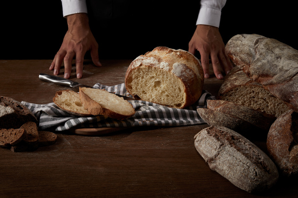 partial view of male baker standing near table with bread, knife and sackcloth - Foto, Bild