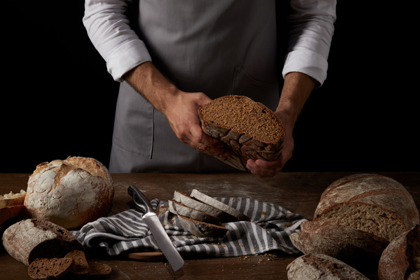 tiro recortado de panadero masculino en delantal sosteniendo el pan sobre la mesa con cuchillo, pan y saco
  - Foto, imagen