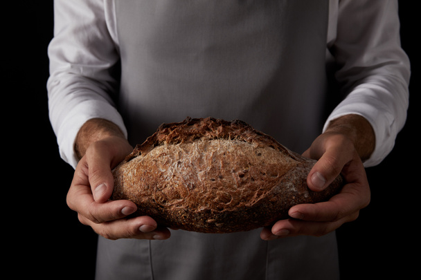 cropped shot of male baker in apron holding bread isolated on black background  - Foto, immagini