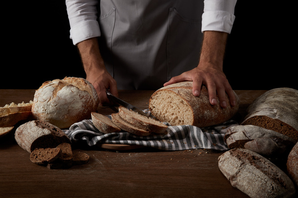 imagen recortada de panadero en delantal corte de pan en el saco en la mesa de madera
  - Foto, Imagen