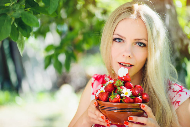 junge zarte blonde Frau mit Erdbeeren in der Schüssel, im grünen Garten ein sonniger Sommertag, warme sommerliche Tonung eines Bildes, Selbstpflege und gesunder Lebensstil. - Foto, Bild