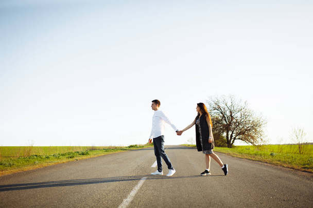 young, happy, loving couple standing on the road holding hands and looking at each other, - 写真・画像