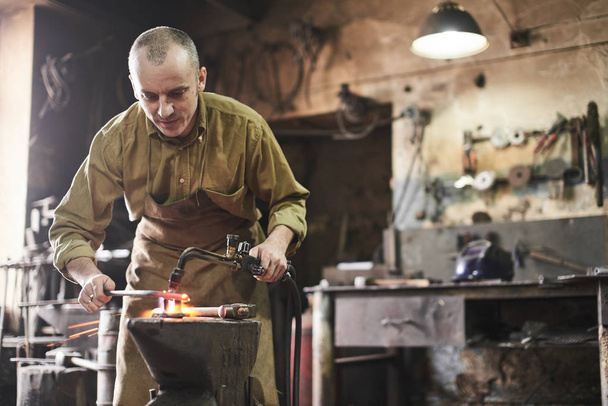 Blacksmith heats the gas burner over metal product on the anvil - 写真・画像