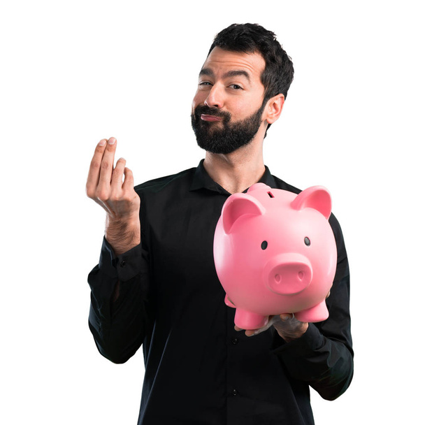 schöner Mann mit Bart hält ein Sparschwein auf weißem Hintergrund - Foto, Bild