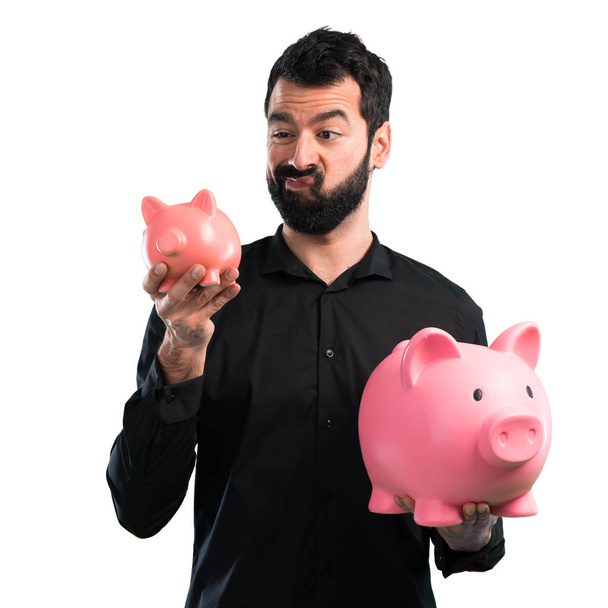 Handsome man with beard holding a piggybank on white background - Foto, Imagen