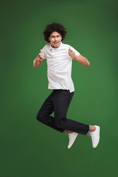 Photo of excited young african curly man jumping isolated over green wall background pointing to you. - Foto, Imagem