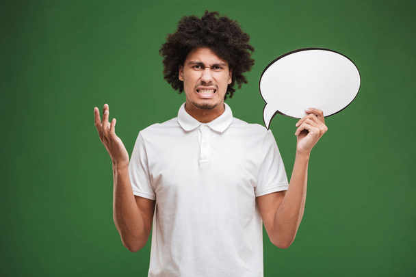 Image of confused young african curly man isolated over green wall background holding speech bubble. - Foto, Bild