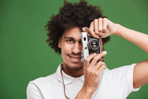 Picture of happy young african curly man photographer isolated over green wall background holding camera. - Valokuva, kuva