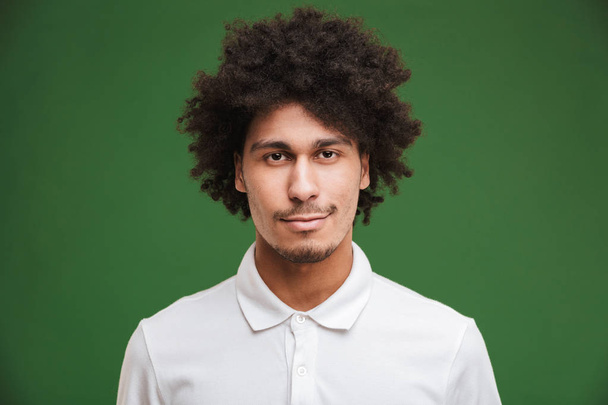 Image of handsome young curly man standing isolated over green wall background looking camera. - Фото, изображение