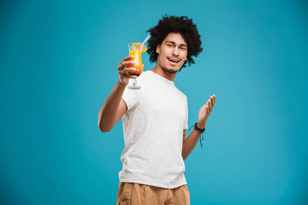Image of excited young african curly man standing isolated over blue background holding cocktail. - Foto, afbeelding