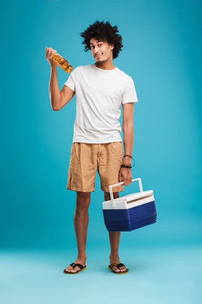 Image of happy young african curly man standing isolated over blue background holding beer. - Фото, изображение