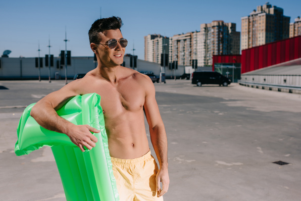 smiling young shirtless man with inflatable bed on parking - Foto, Imagen