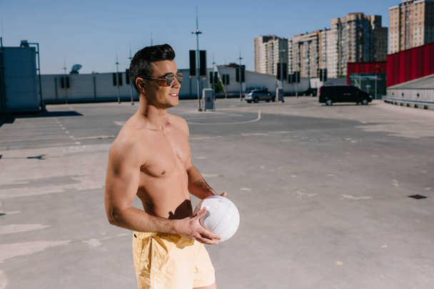 駐車場でバレーボールのボールを保持している幸せの上半身裸の男 - 写真・画像