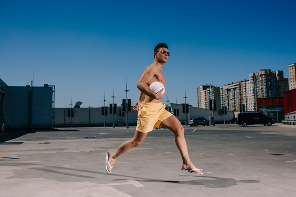 молодий без сорочки чоловік біжить з волейбольним м'ячем на парковці
 - Фото, зображення