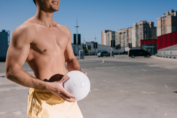 plan recadré d'un jeune homme torse nu tenant une balle de volley-ball sur un parking
 - Photo, image