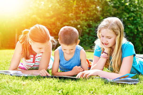Friends reading books outdoori on grass in summer day - Fotografie, Obrázek