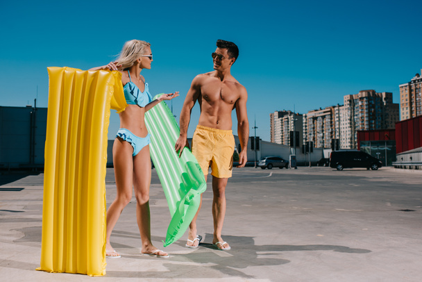 attractive young couple in beach clothes with inflatable beds on parking - Photo, Image