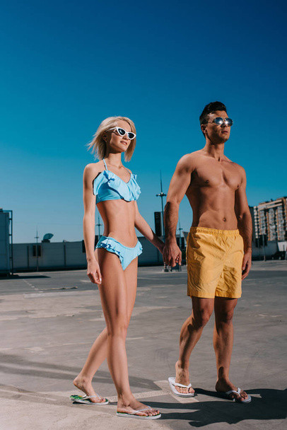 young couple in beach clothes holding hands and walking on parking - Foto, imagen