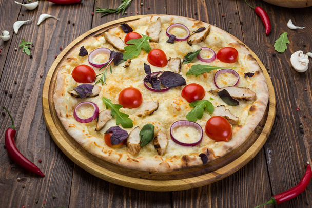 鶏、チェリー トマト、チーズ、玉ねぎで飾られたボード上とイタリアのピザは、ルッコラとバジルの葉します。 - 写真・画像