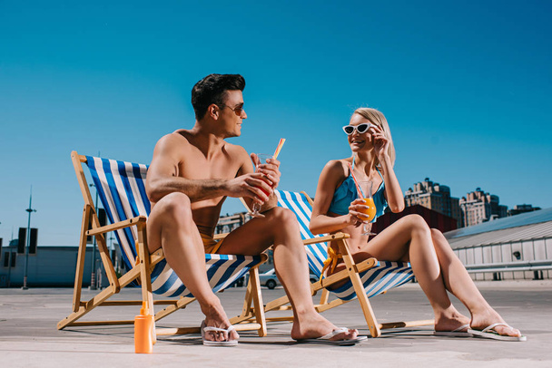 young couple with refreshing cocktails sitting on sun loungers on parking - Foto, afbeelding