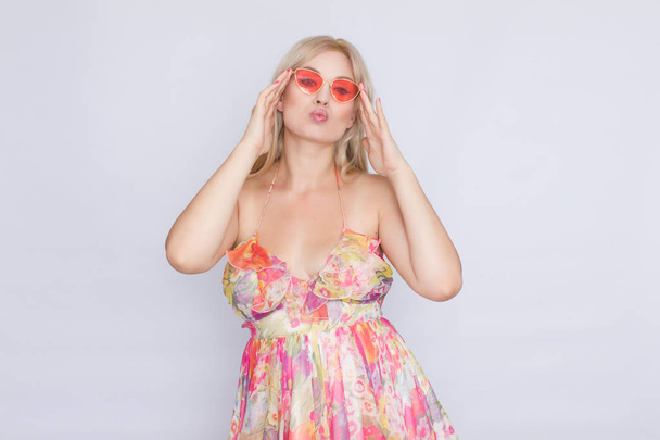 portrait of a young blond woman with long hair in a floral pink dress, and bright pink sunglasses - Foto, Bild