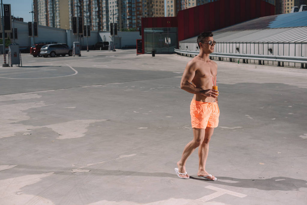 bonito jovem sem camisa homem em calções de natação com coquetel no estacionamento
 - Foto, Imagem