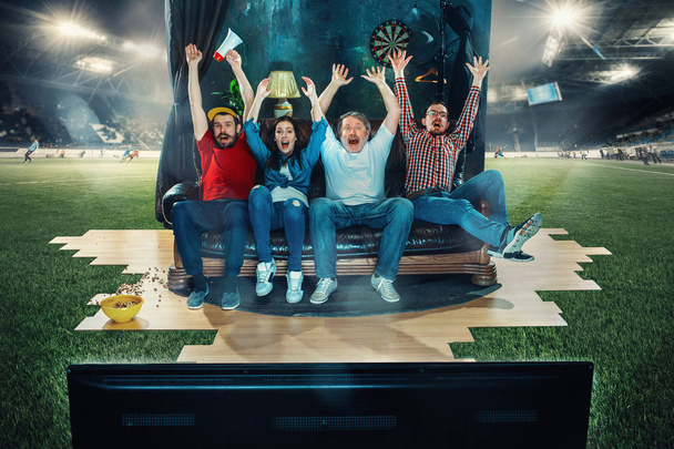 Soccer football fans sitting on the sofa and watching TV in the middle of a football field. - 写真・画像