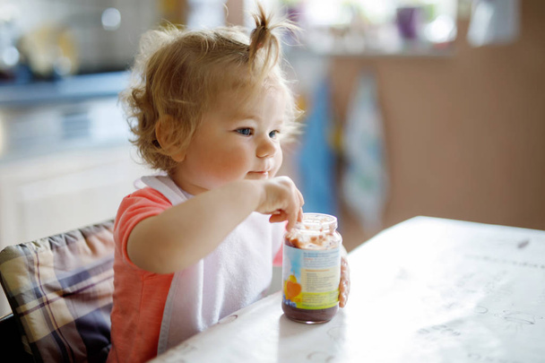 Очаровательная девочка ест из ложечных овощей или фруктовых консервов, ребенок, кормление и концепция развития
. - Фото, изображение