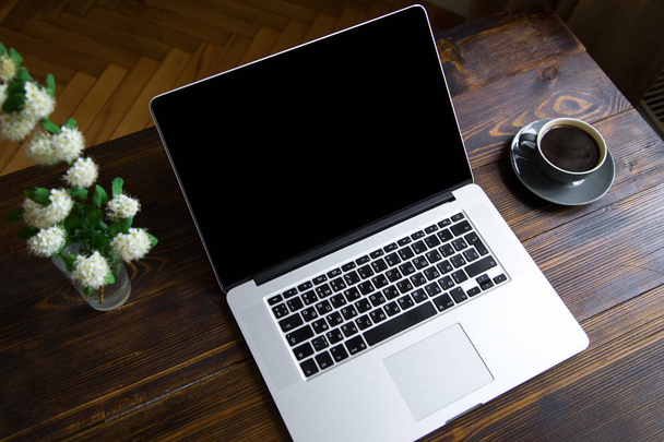 laptop with coffee cup and vase with white flowers on vintage wooden table, concept of blogger workspace  - Photo, image