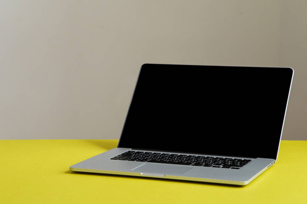 grey opened laptop with black screen on bright olive yellow background, concept of female blogger workspace  - Фото, изображение