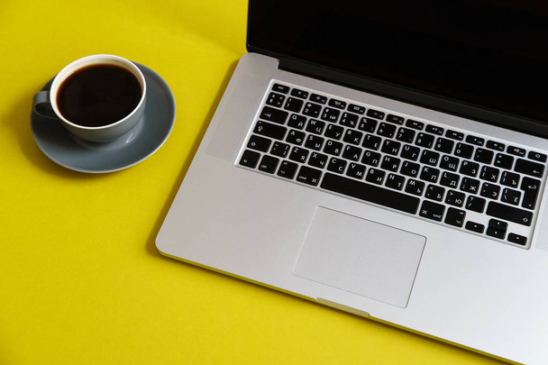 grey opened laptop with hot coffee in cup on bright olive yellow background, concept of female blogger workspace  - Fotó, kép