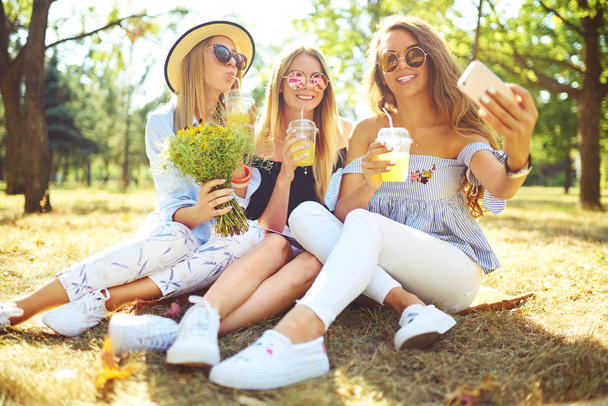 Three nice girls  having fun In the park and make selfie. Excellent sunny weather. Beautiful figures. Super mood. Summer concept. - Fotoğraf, Görsel