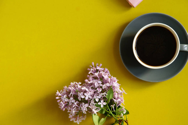 beautiful lilac flowers and pink notebook with coffee cup on yellow background, concept of spring female blogger workspace  - 写真・画像