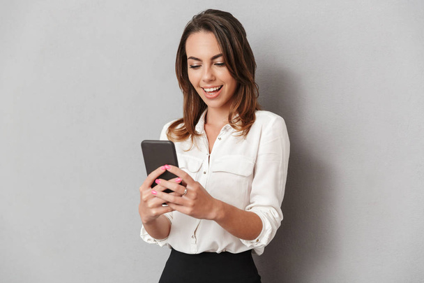 Portrait of a cheerful young business woman using mobile phone isolated over white background - Zdjęcie, obraz