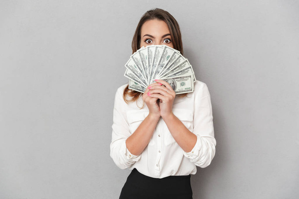 Portrait of a happy young business woman holding bunch of money banknotes at her face isolated over white background - Foto, Bild