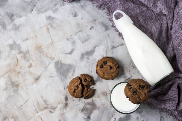 Μπισκότα σοκολάτας δίπλα σε ένα γυάλινο μπουκάλι και ένα ποτήρι γάλα σε ένα γκρι τραπέζι. Βάλτε το Top view, επίπεδη, αντίγραφο χώρου - Φωτογραφία, εικόνα